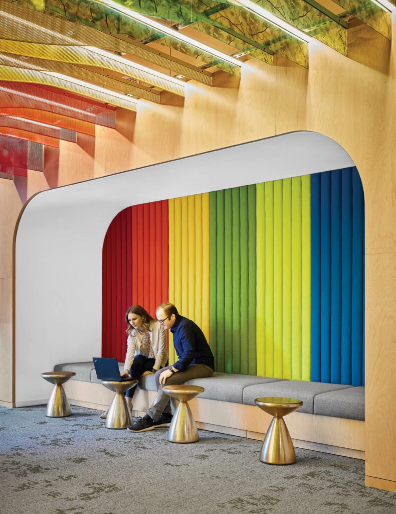 two people sit on a bench in front of a rainbow wall installation