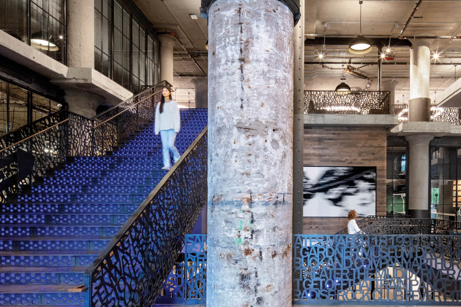 a woman walks down a blue staircase next to balustrades composed of letters