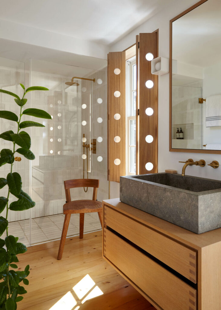 a primary bathroom with light wood cabinets and a row of wall sconces