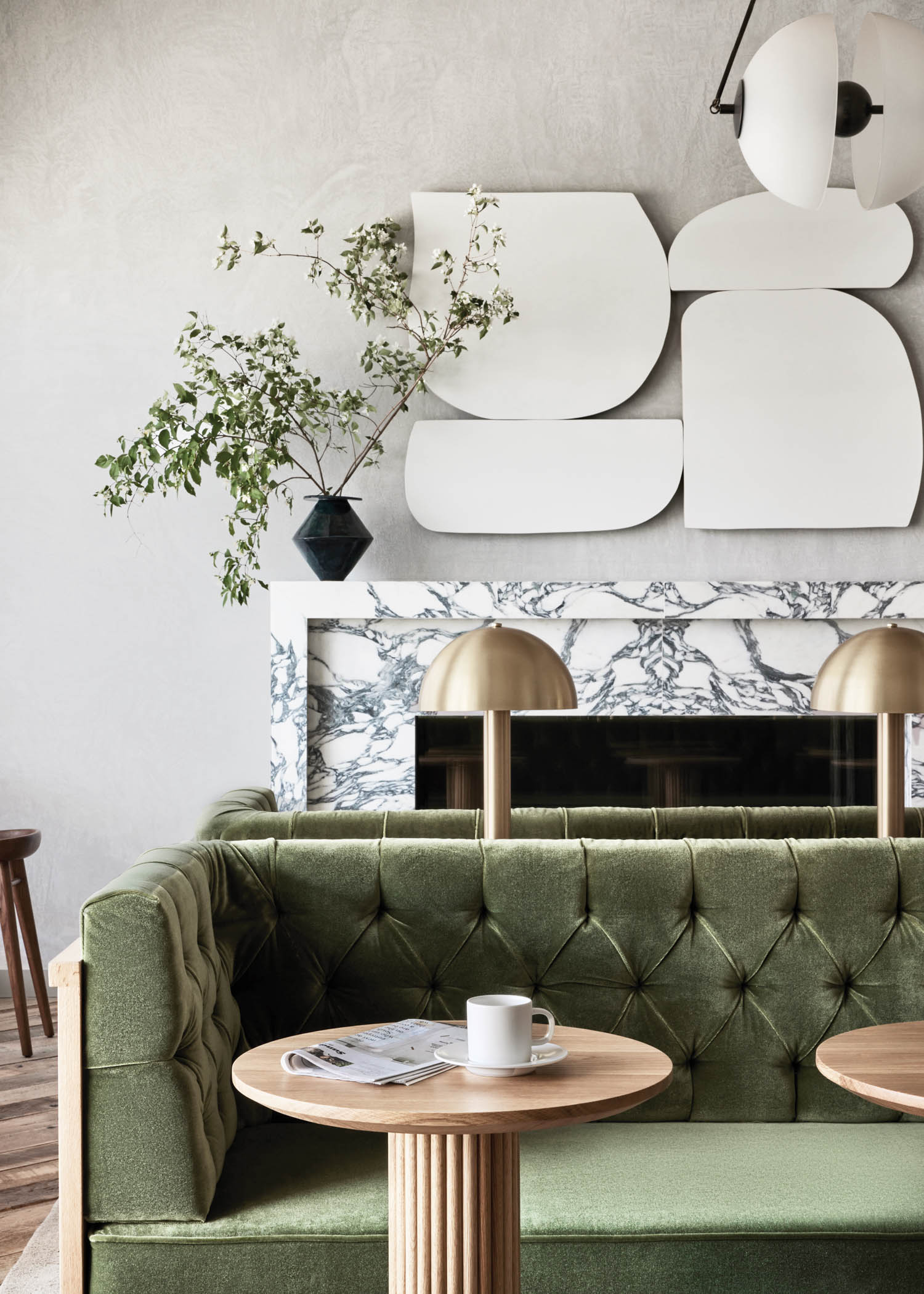 an emerald velvet couch in front of a black and white marbled fireplace