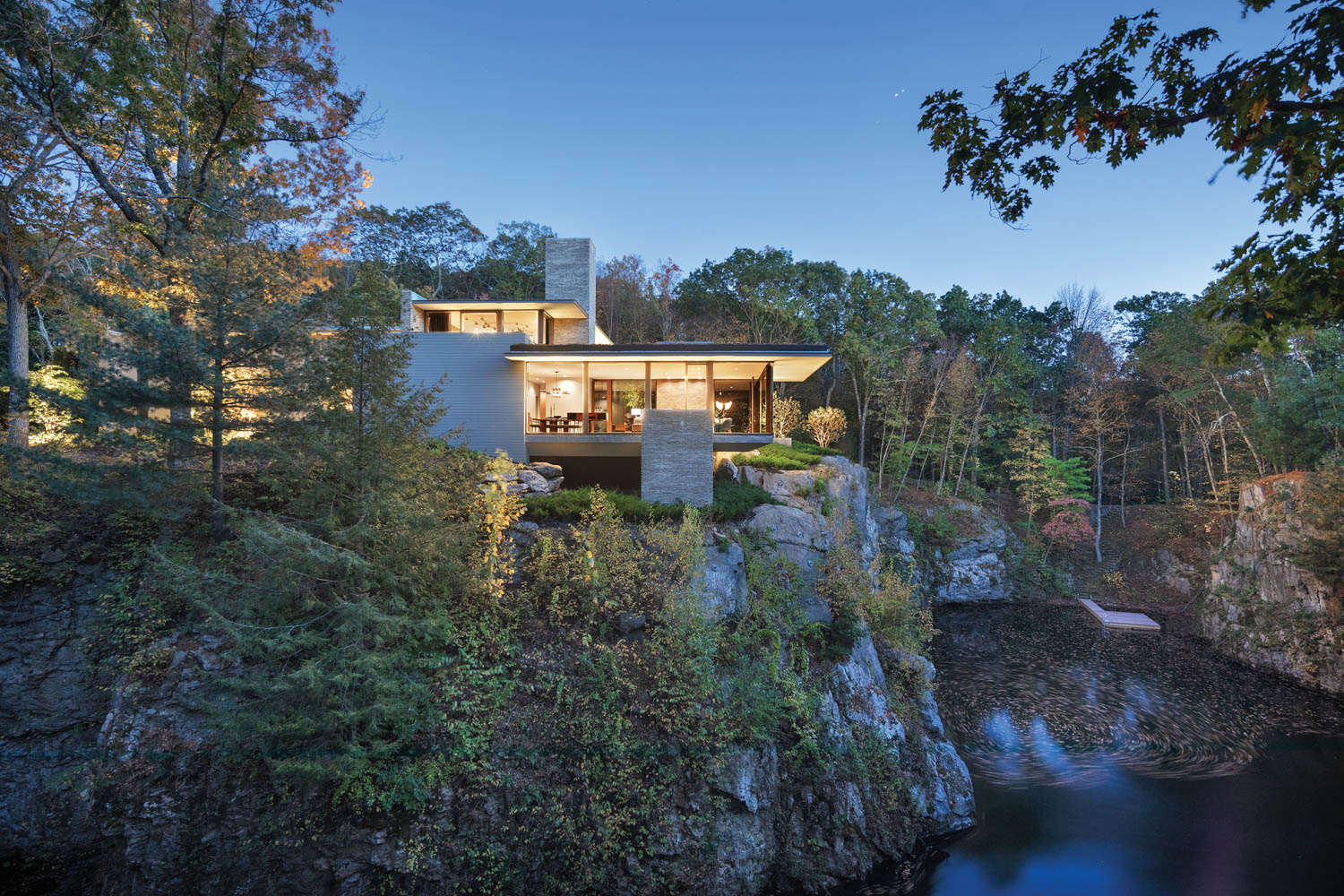 a modern house sits on the rocky edge of a lake at night