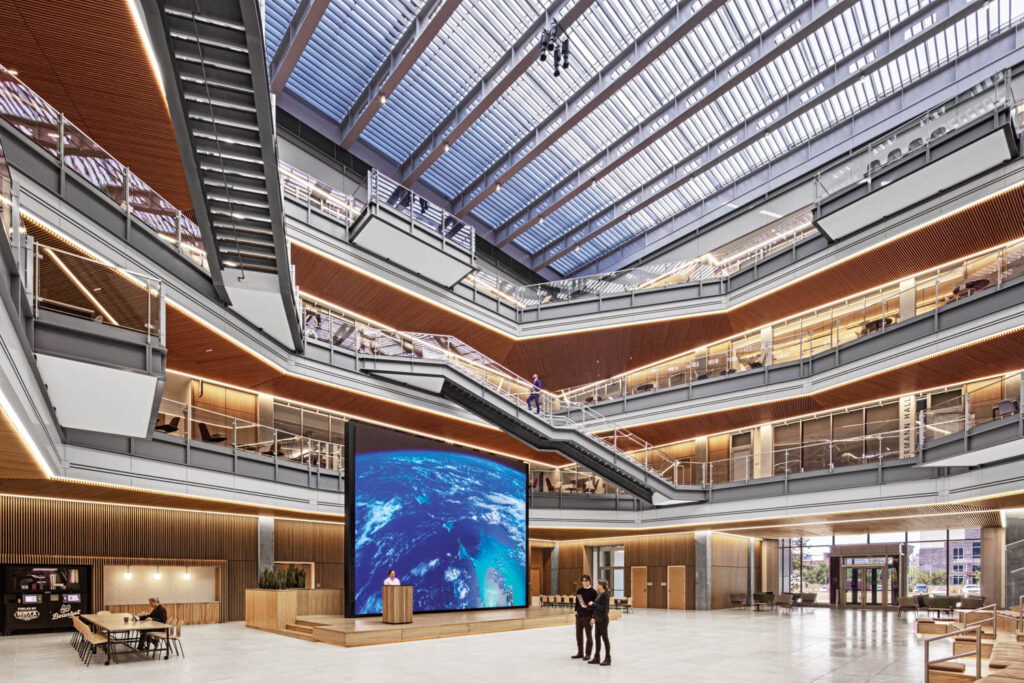 large atrium with multiple stairways and large LED screen on top of a wooden platform