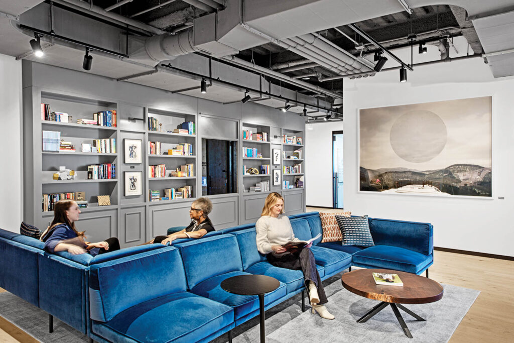 a woman sits on a blue velvet sofa in an office