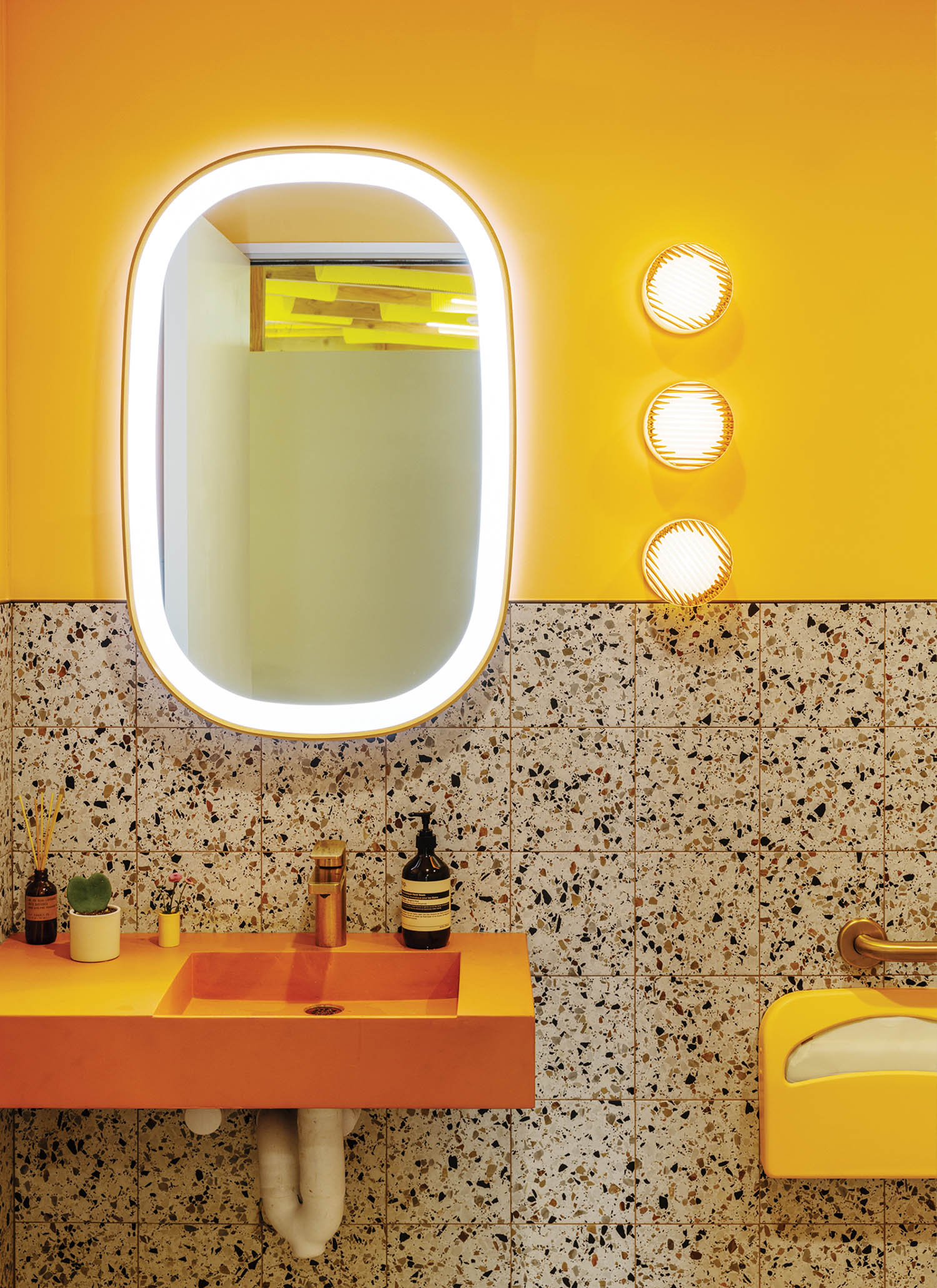 bathroom with yellow walls, lit mirror and orange sink